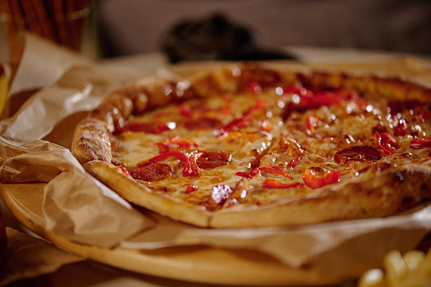 Close-up image showcasing pepperoni pizza with bell pepper slices on rustic wooden board cradled by parchment paper giving a warm and inviting look