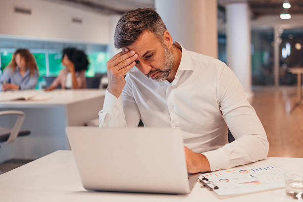 istock Stressed businessman having headache while working on laptop in office 2212461486