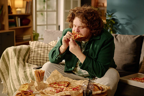 istock Man Enjoying Pizza While Sitting on Couch at Home 2212461521