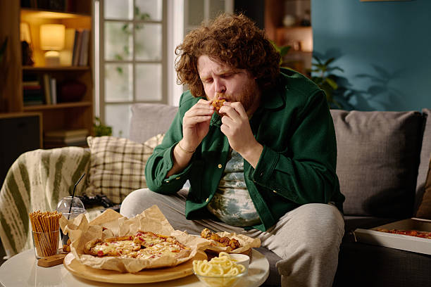 istock Man Enjoying Pizza While Sitting on Couch in Cozy Room 2212461920