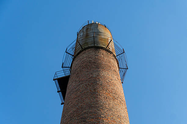 istock A tall brick chimney tower rises against a bright blue sky, featuring a metal spiral staircase along its side, highlighting industrial architecture 2212462263