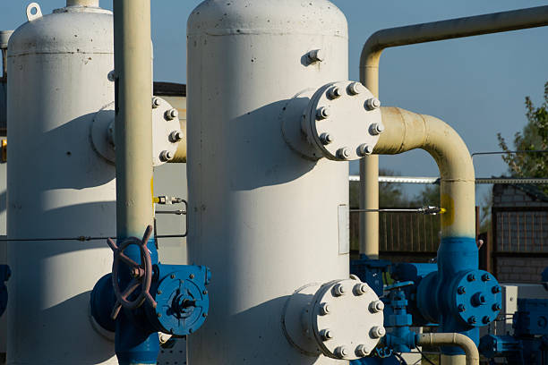 Large white storage tanks with blue pipelines at a gas facility reflecting sunlight, indicating active industrial operations