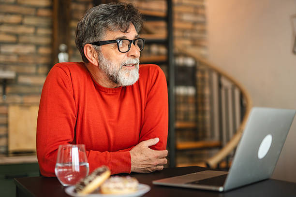 istock senior man use laptop with doughnut on table and sit in the kitchen 2212464352