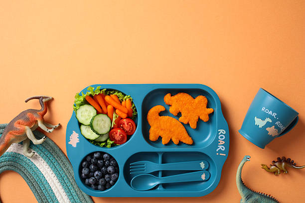 istock Creative kid's lunch tray with dino nuggets, veggies, and berries. Flat lay, top view. 2212465596