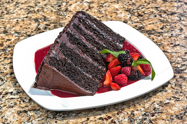 Chocolate cake decorated with chocolate chips, accompanied with red berry sauce and served with red berries
