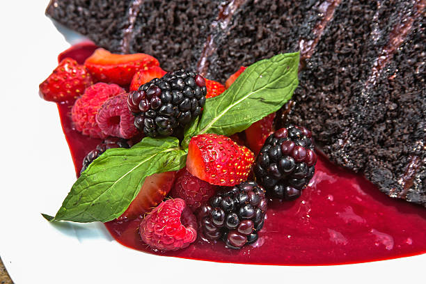 Chocolate cake decorated with chocolate chips, accompanied with red berry sauce and served with red berries