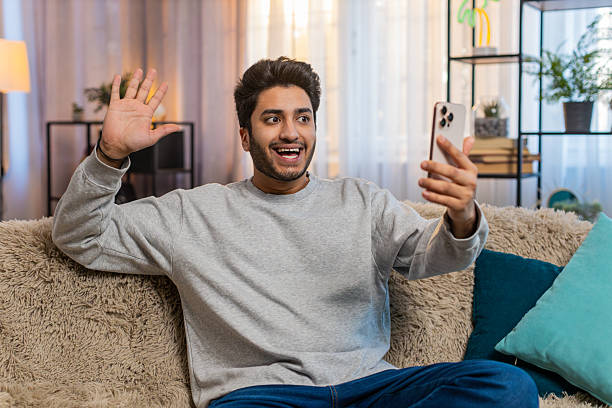 istock Indian man making video call with wave chatting with friend on smartphone sitting on sofa at home 2212473893