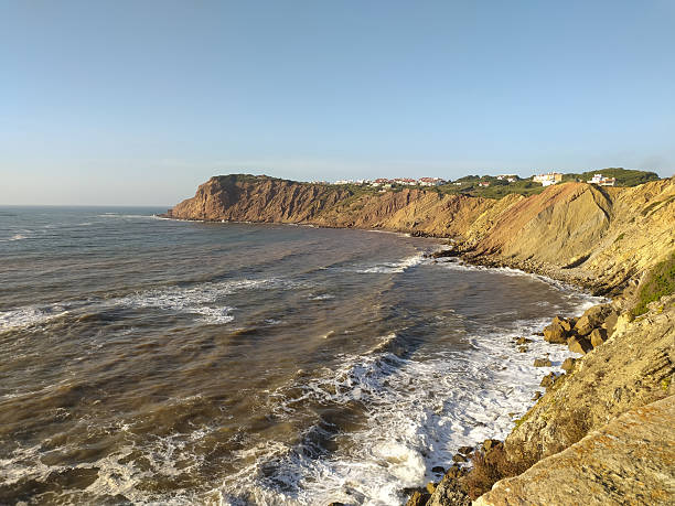 Dramatic coastal scene featuring rugged cliffs meeting the turbulent ocean under a clear sky. Evokes themes of natures power and serene beauty, ideal for travel or environmental projects.