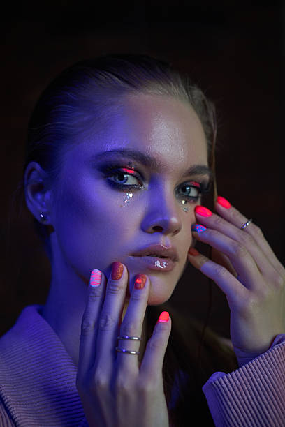 istock woman poses with intricate nail art and striking neon makeup while soft light enhances her features. contrasting colors create a bold and alluring atmosphere in the studio 2212484052