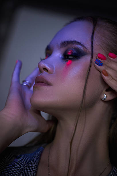 istock model poses elegantly with intricate makeup and vibrant nail colors in a dimly lit studio. focus is on her facial features, highlighting artistic makeup and stylish nail designs 2212484067