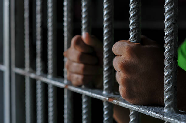 istock hands of a prisoner behind prison bars on black background 2212489845