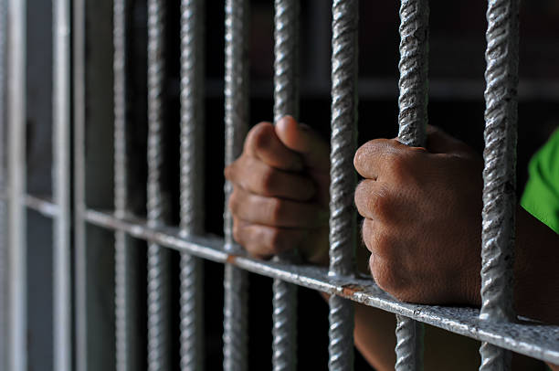 istock hands of a prisoner behind prison bars on black background 2212489849