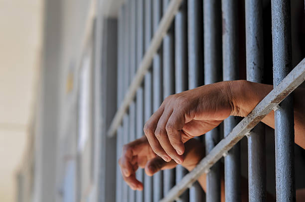 istock hands of a prisoner behind prison bars on black background 2212489953