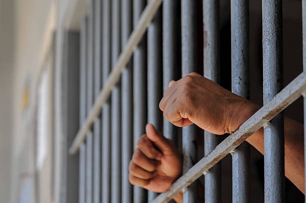 istock hands of a prisoner behind prison bars on black background 2212489982