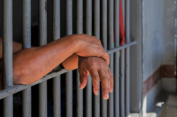 istock hands of a prisoner behind prison bars on black background 2212489983