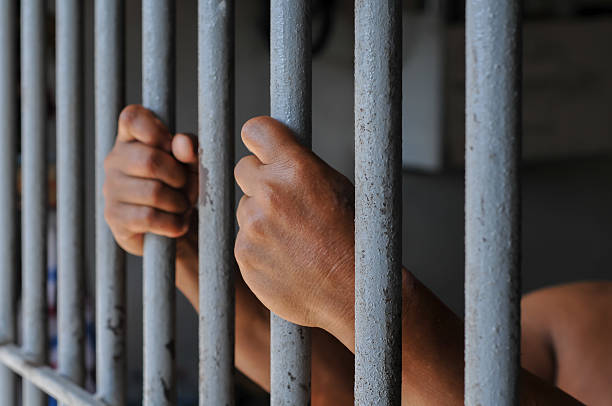 istock hands of a prisoner behind prison bars on black background 2212490020