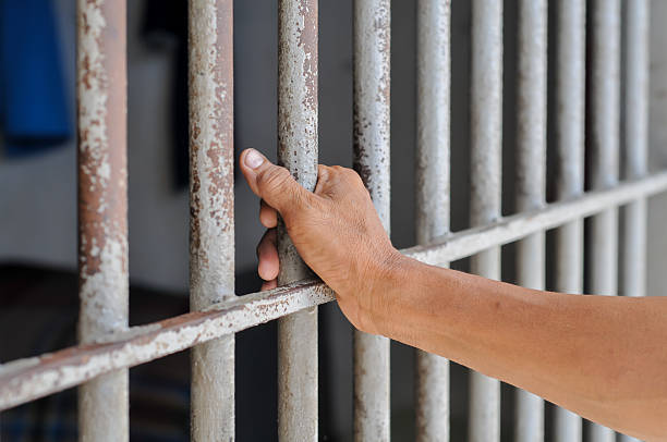 istock hands of a prisoner behind prison bars on black background 2212490027