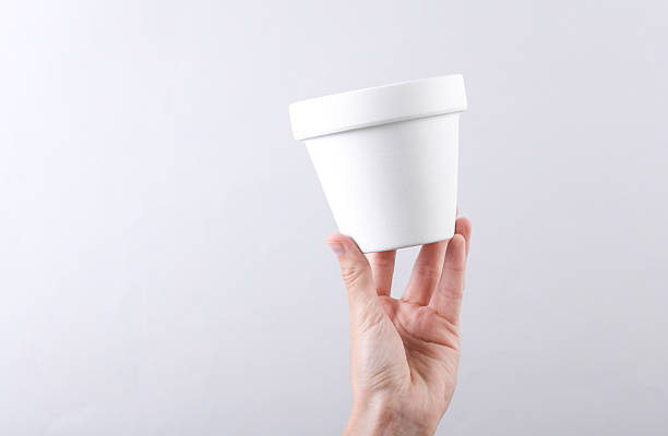 Hand holding white clay flower pot on grey background
