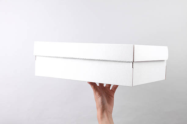 istock Female hand holding white cardboard box on grey background 2212497603