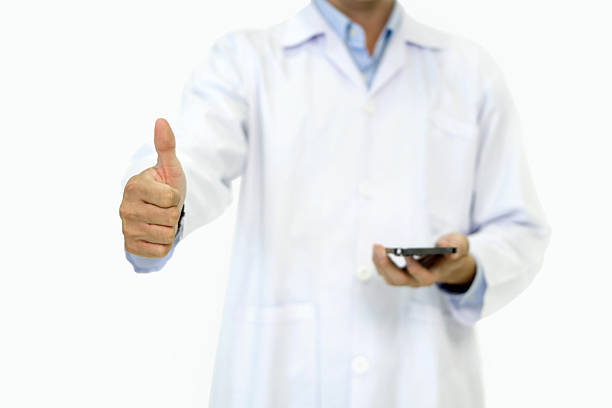 Doctor or scientist in a white lab coat standing with finger thumbs up while holding smartphone with his hand. Portrait on white background, studio shot.