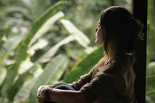 Woman Sitting by Window Looking at Tropical Nature