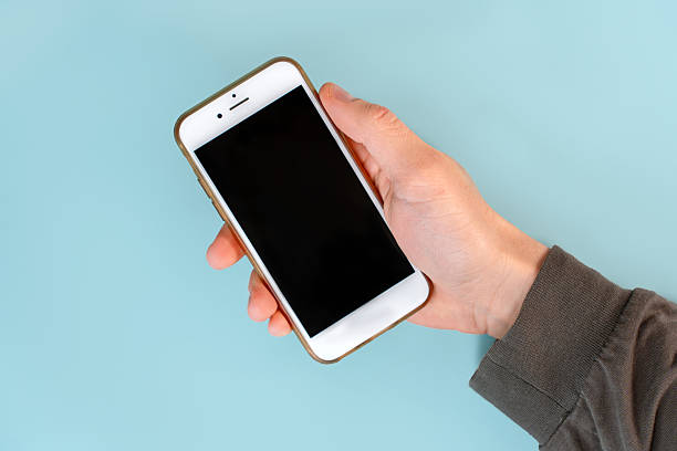 istock The man's hands are holding a smartphone with a black screen on a blue table background. Close up, point of view shot. 2212503756