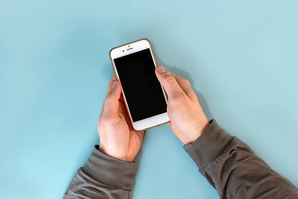 istock The man's hands are holding a smartphone with a black screen on a blue table background. Close up, point of view shot. 2212503772