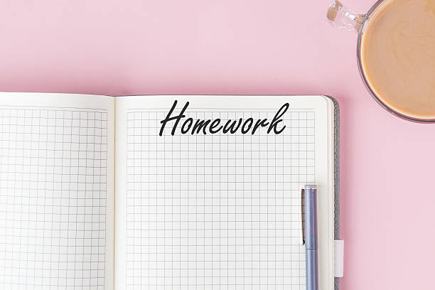 istock Open squared notebook with title homework, blue pen clipped to the side, and cup of coffee on pastel pink background, minimalist stylish composition concept education 2212509877