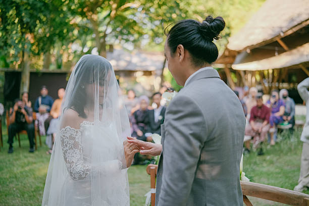 istock Asian Bride Putting Ring on Groom During Outdoor Ceremony 2212511937