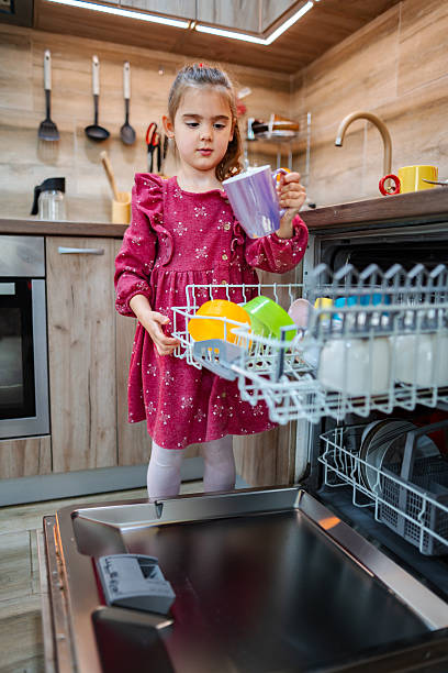 istock Little girl loading the dishwasher in a modern kitchen 2212512184