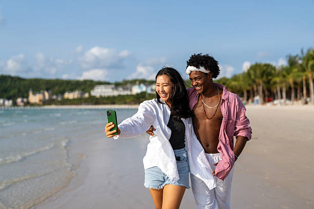 istock Happy interracial couple taking selfie at a tropical beach enjoying vacation, remote work 2212512596