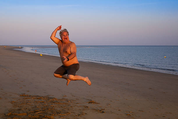 A joyful middle-aged man jumps on the sand at Isla Canela beach in Huelva, Spain, showing fun and carefree energy during a summer afternoon. This lively beach scene is ideal for lifestyle, humor, and vacation themes.