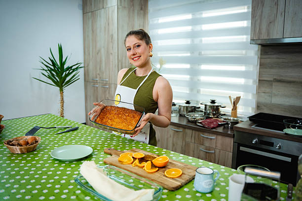 istock Woman holding orange cake in kitchen with ingredients on table 2212519422