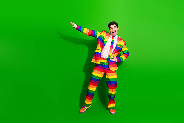 istock Vibrant young man in rainbow-colored suit posing joyfully in front of a bright green background, expressing celebration and positivity. 2212520366