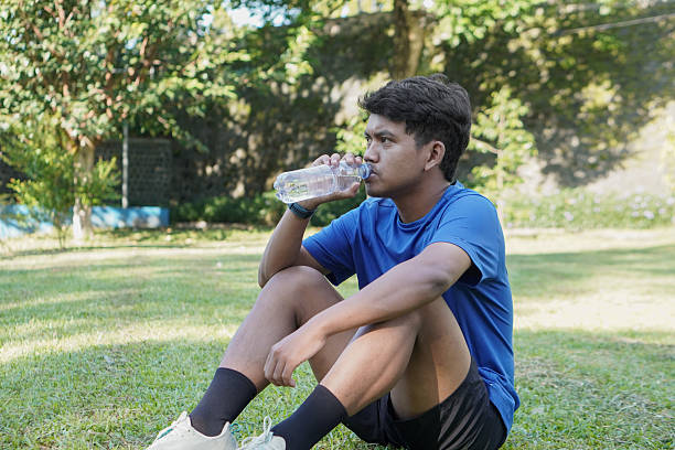 istock Asian man taking a break after jogging in a city park, drinking water from a plastic bottle, looking refreshed and relaxed 2212521145