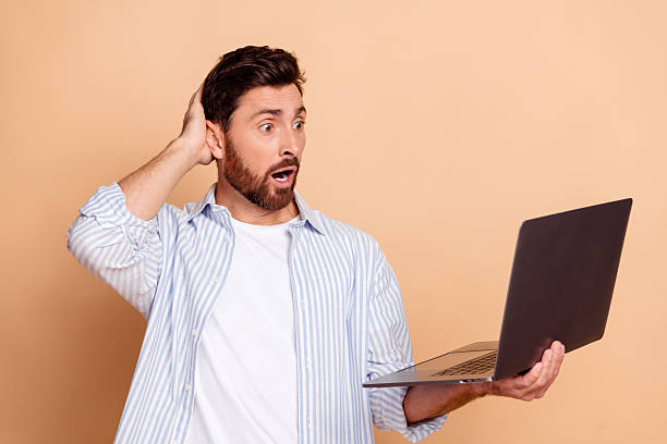 istock Surprised young man holding a laptop expresses shock at a surprising discovery, dressed casually 2212523864