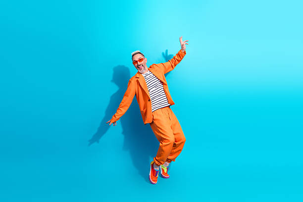 istock Charismatic middle aged man in vibrant orange suit posing joyfully against a bright blue background 2212524191