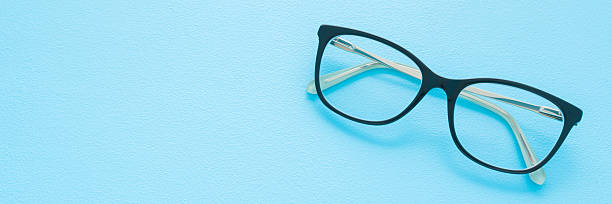 istock Eyeglasses with dark black plastic frame on light blue table background. Pastel color. Wide banner. Closeup. Empty place for text. Top down view. 2212524504