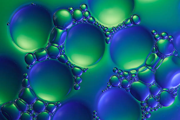 Essence liquid sample on water background with blue and green light reflecting on the surface of water bubbles. Tiny bubbles cling to form large, dense bubbles. Beauty product moisture ingredient.