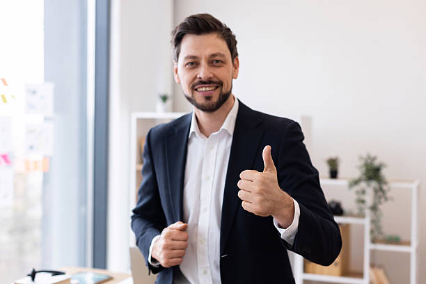 istock Smiling businessman showing thumbs up gesture in modern office environment 2212527672