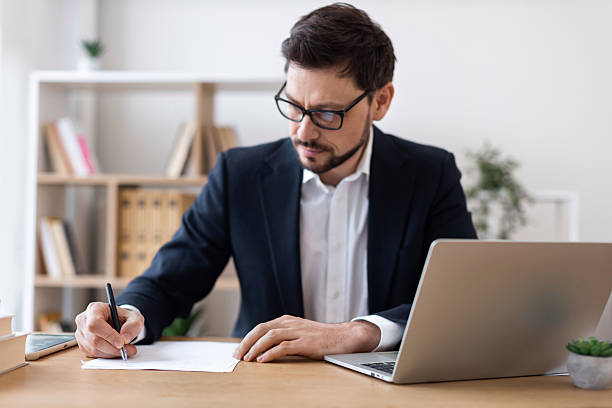 istock Professional businessman writing and working on documents at desk with laptop 2212527764