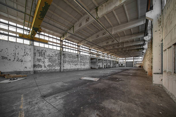 istock Empty factory hall with peeling walls, exposed beams, and large windows letting in dim light 2212529742