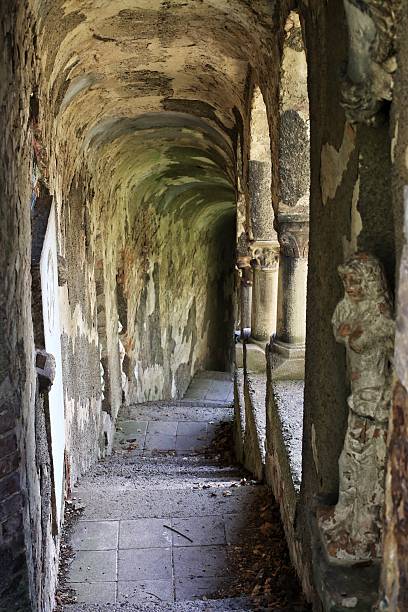 istock Weathered stone corridor lined with statues and flaking walls in dim, narrow passageway 2212529964