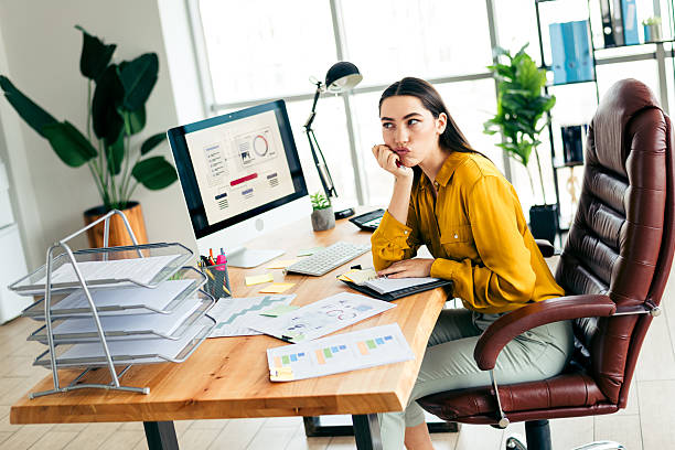 istock Young professional businesswoman pondering ideas at modern office workstation with documents and workstation under daylight 2212531958