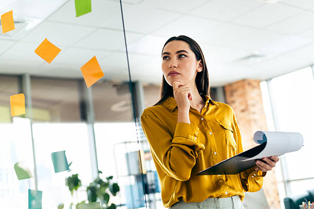 istock Young professional woman in a modern office environment analyzing ideas on a glass board during a creative planning session 2212532081