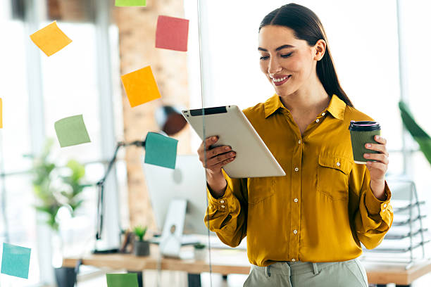 istock Confident professional woman multitasking in a modern office with a tablet and coffee, surrounded by colorful sticky notes on a bright day. 2212532088