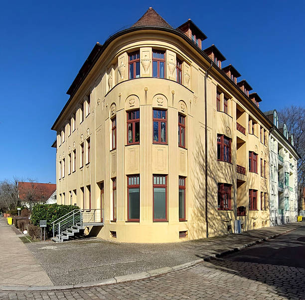 istock Listed monument in Magdeburg, Germany - Corner building facade with red window frames, and curved architectural details 2212532245