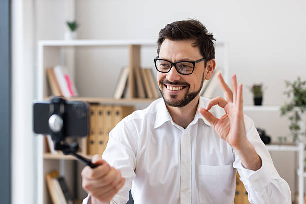 istock Man video calling with smartphone indoors wearing glasses smiling and gesturing 2212532962