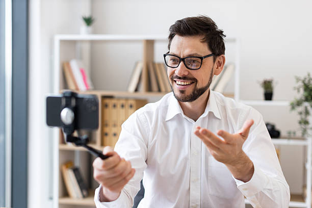istock Man video calling with smartphone indoors wearing glasses smiling and gesturing 2212532965