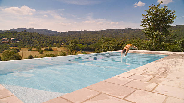 A Woman Dives Headfirst into a Beautiful Infinity Pool,Surrounded by Nature and Overlooking a Lush,Scenic Valley. The Sunlight Sparkles on the Water's Surface as she Enjoys a Refreshing Plunge During a Warm Summer Day. The Setting Captures a Perfect Blend of Adventure,Freedom,and Tranquil Natural Beauty